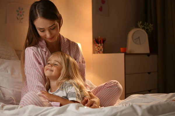 Happy woman with her little daughter on bed in evening — Stock Photo, Image