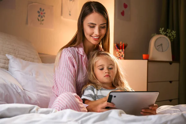 Femeia fericită și fiica ei mică cu calculator tabletă pe pat seara — Fotografie, imagine de stoc