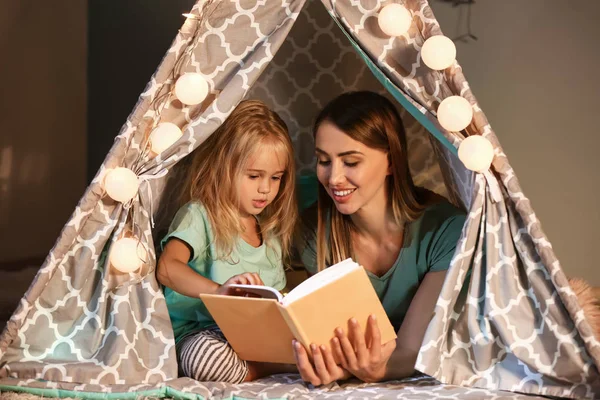 Lycklig kvinna med sin lilla dotter läsning bok i kyffe hemma — Stockfoto