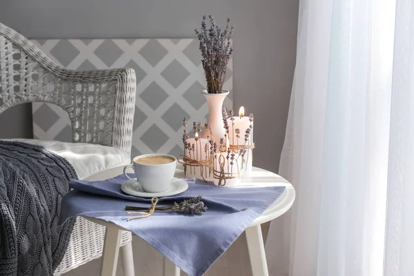 Cup of coffee, burning candles and lavender on table in room