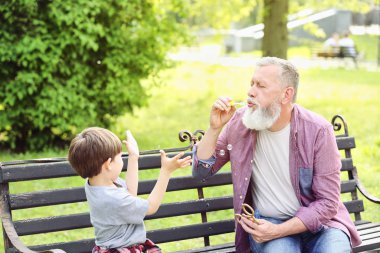 Sevimli küçük çocuk ve dedesi parkta sabun kabarcıkları üfleme