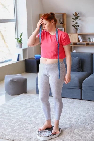 Overweight woman with measuring tape standing on scales at home. Weight loss concept