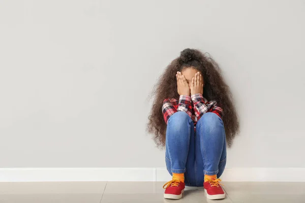 Offended African-American girl sitting on floor near light wall — Stock Photo, Image