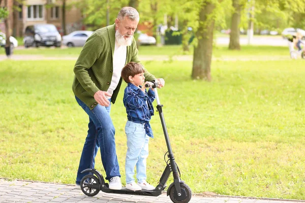 Aranyos kisfiú nagypapa lovaglás kick robogó Park — Stock Fotó