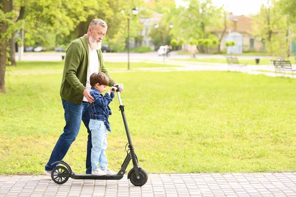 Lindo niño pequeño con abuelo montando patinete scooter en el parque —  Fotos de Stock
