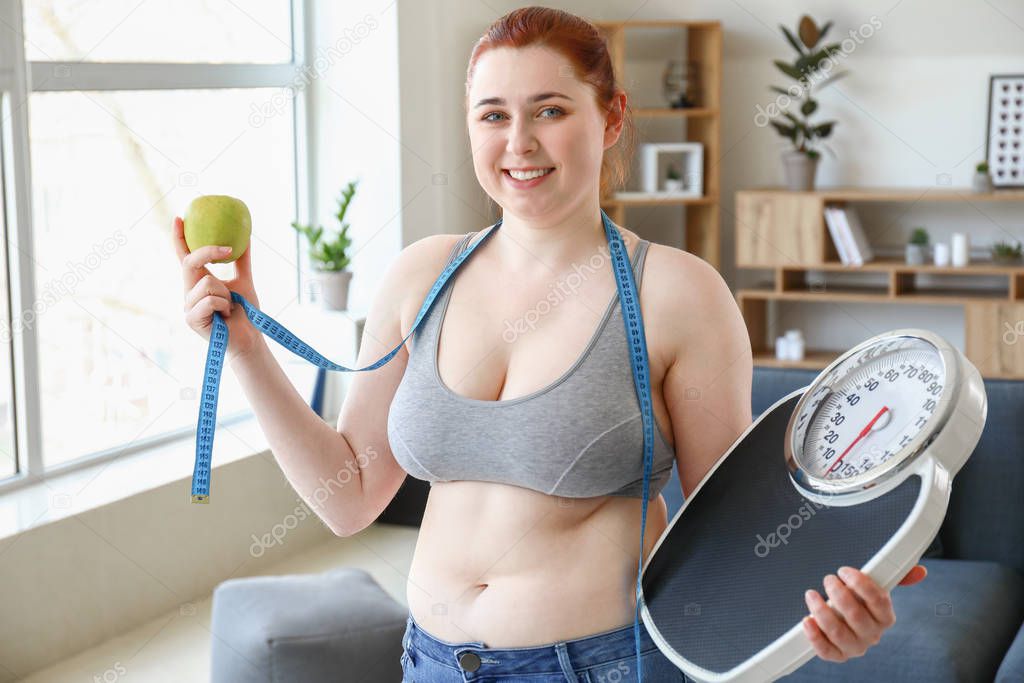 Overweight woman with measuring tape, apple and scales at home. Weight loss concept