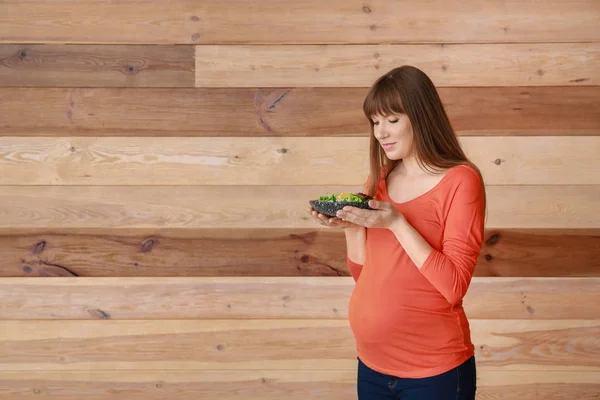 Beautiful pregnant woman with healthy salad on wooden background — Stock Photo, Image