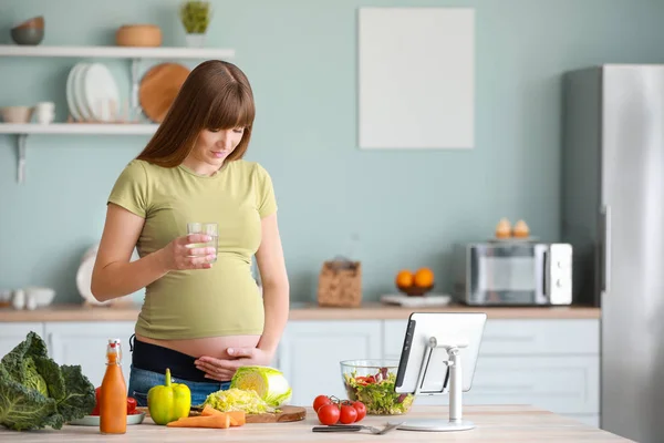 Красивая беременная женщина со стаканом воды на кухне — стоковое фото