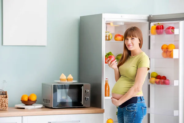 Wanita hamil yang cantik memilih makanan di lemari es dapur — Stok Foto