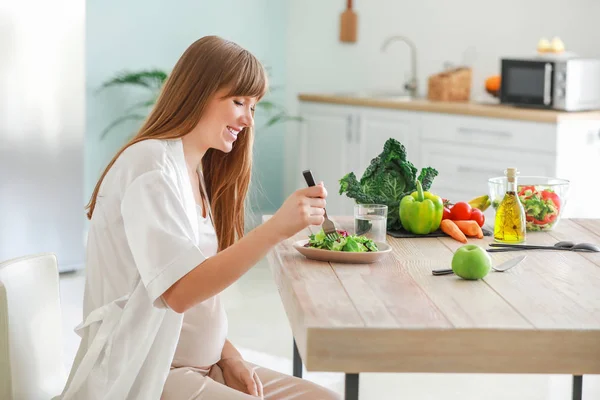 Hermosa mujer embarazada comiendo ensalada saludable en la cocina —  Fotos de Stock