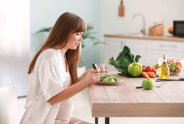 Hermosa mujer embarazada comiendo ensalada saludable en la cocina —  Fotos de Stock