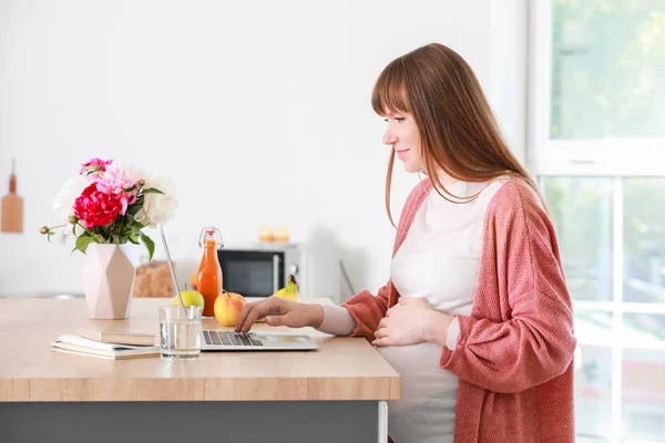 Beautiful pregnant woman with laptop in kitchen — Stock Photo, Image