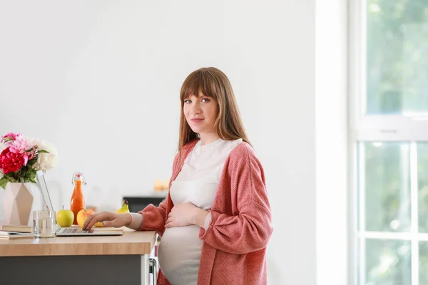 Beautiful pregnant woman with laptop in kitchen — Stock Photo, Image