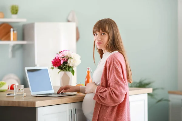 Beautiful pregnant woman with laptop in kitchen — Stock Photo, Image