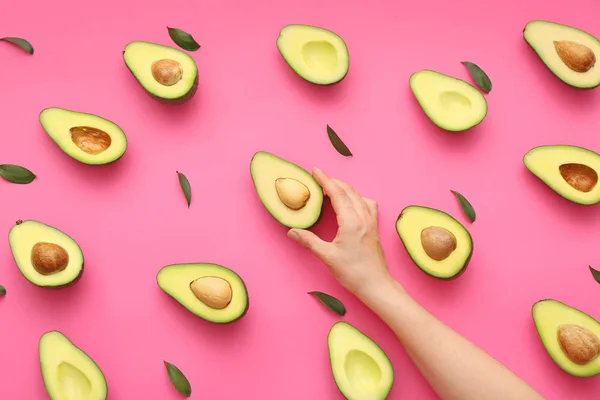 Female hand and halves of fresh avocados on color background — Stock Photo, Image