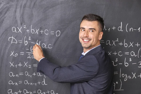 Guapo profesor de matemáticas escribiendo en pizarra en el aula — Foto de Stock