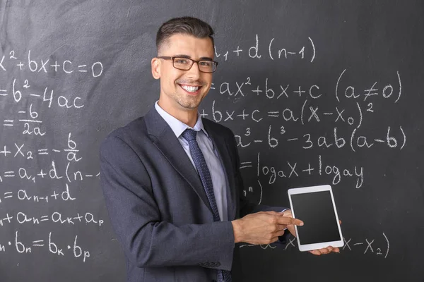 Profesor de matemáticas guapo con tableta cerca de pizarra en el aula — Foto de Stock