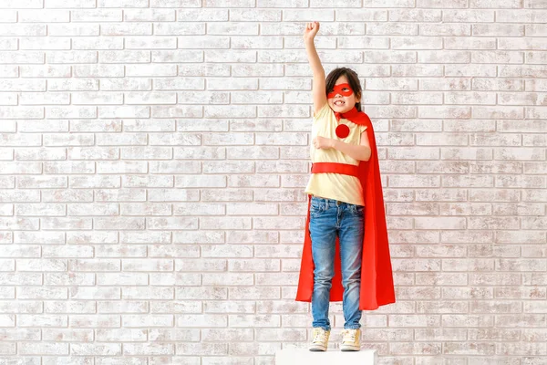Linda niña vestida como superhéroe cerca de la pared de ladrillo — Foto de Stock