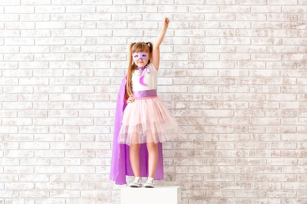 Menina bonito vestido como super-herói perto da parede de tijolo — Fotografia de Stock