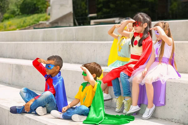 Cute little children dressed as superheroes sitting on stairs outdoors — Stock Photo, Image