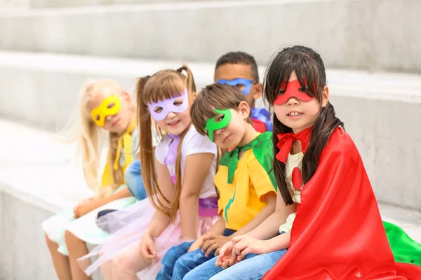 Niedliche kleine Kinder, die als Superhelden verkleidet auf Treppen im Freien sitzen — Stockfoto