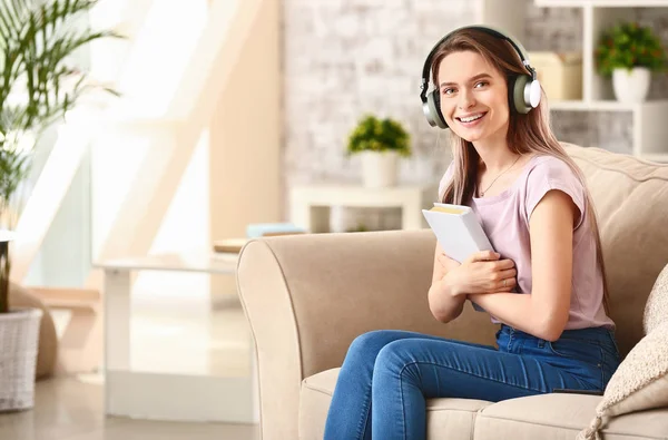Красивая молодая женщина слушает аудиокнигу, сидя дома на диване — стоковое фото