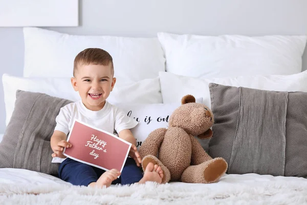 Cute little boy with greeting card for Father's Day on bed — Stock Photo, Image