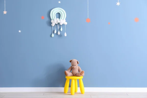 Taburete con juguete oso cerca de la pared de color en la habitación de los niños — Foto de Stock