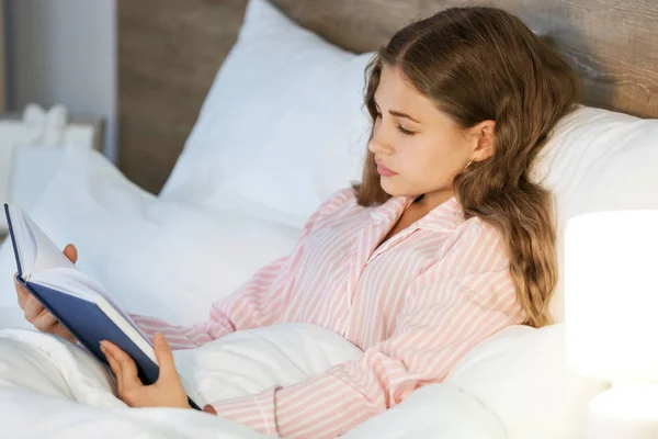 Teenage girl reading book in bed at night — Stock Photo, Image