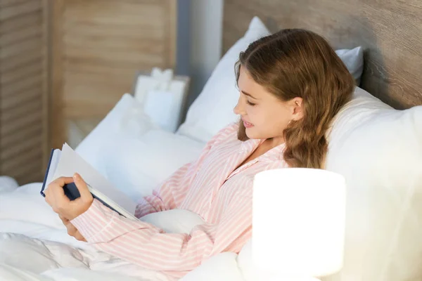 Teenage girl reading book in bed at night — Stock Photo, Image