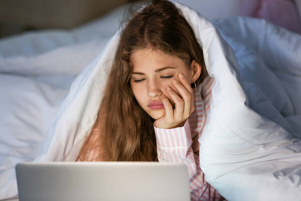Tired teenage girl with laptop in bed at night