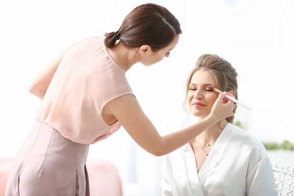 Artista de maquiagem profissional trabalhando com a jovem noiva em casa — Fotografia de Stock