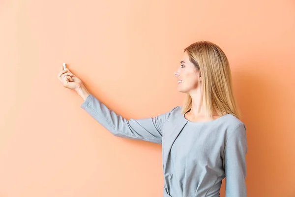 Beautiful female teacher writing something against color background — Stock Photo, Image