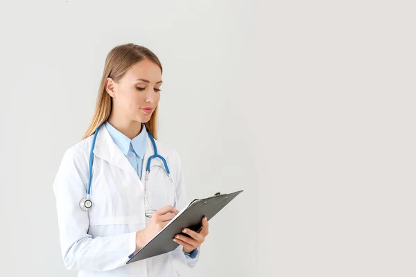 Female doctor with stethoscope and clipboard on light background — Stock Photo, Image