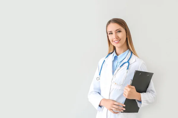 Médica com estetoscópio e prancheta em fundo claro — Fotografia de Stock