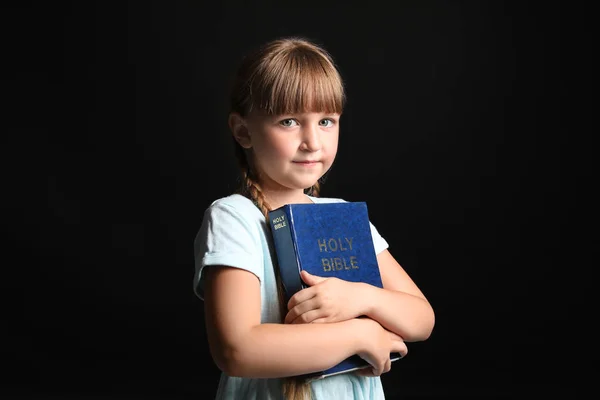 Kleines Mädchen mit Bibel auf dunklem Hintergrund — Stockfoto