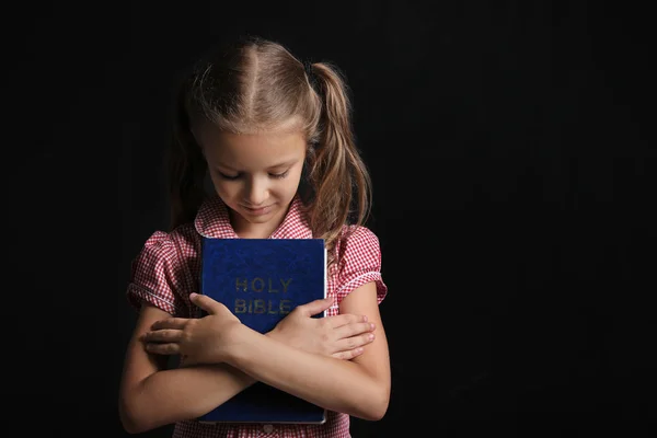 Roztomilá holčička s Biblí na tmavém pozadí — Stock fotografie