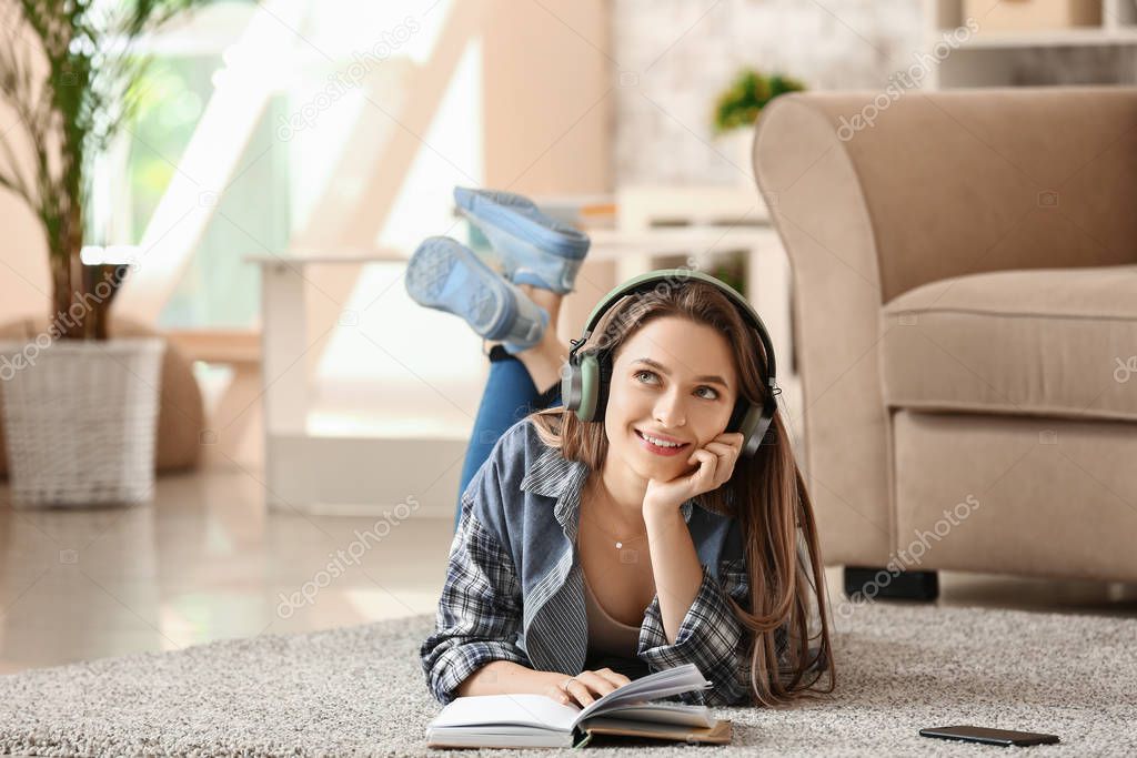 Beautiful young woman listening to music while reading book at home