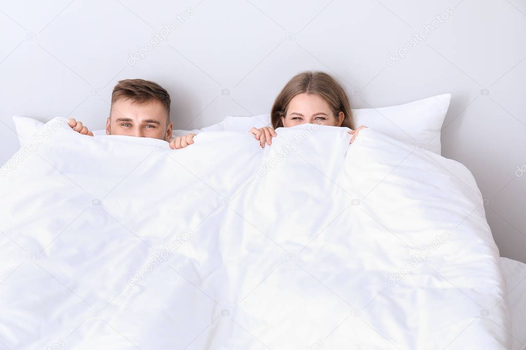 Portrait of young couple hiding under blanket in bedroom