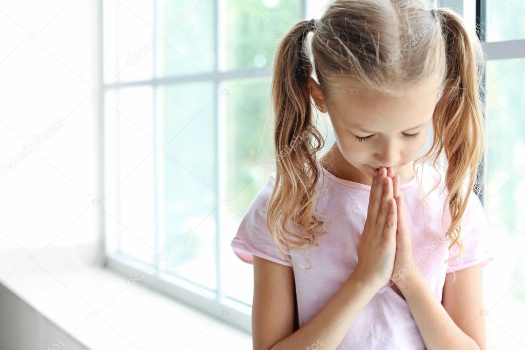 Praying little girl near window