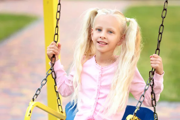 Carino bambina che gioca su altalene nel parco — Foto Stock