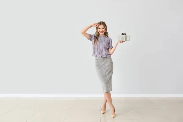 Mooie jonge vrouw met geschenk doos tegen lichte muur — Stockfoto