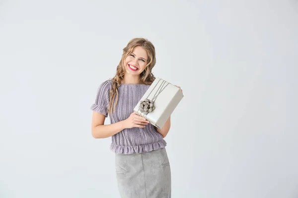 Beautiful young woman with gift box on light background — Stock Photo, Image