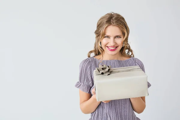 Schöne junge Frau mit Geschenkbox auf hellem Hintergrund — Stockfoto