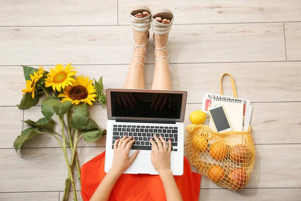 Vrouw met laptop, zonnebloemen en boodschappentas zittend op de vloer, bovenaanzicht — Stockfoto