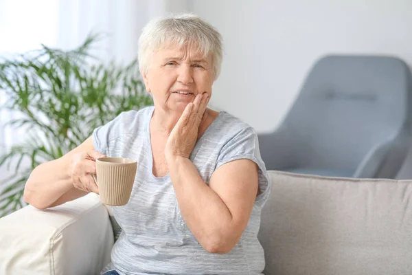 Ηλικιωμένη γυναίκα με ευαίσθητα δόντια και φλιτζάνι ζεστό καφέ στο σπίτι — Φωτογραφία Αρχείου