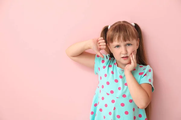 Little girl suffering from toothache and showing thumb-down gesture on color background — Stock Photo, Image