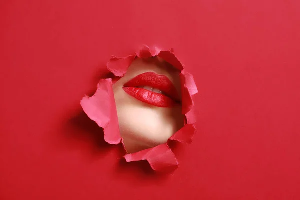 Usta pięknej młodej kobiety widoczne przez otwór w kolorowym papierze — Zdjęcie stockowe