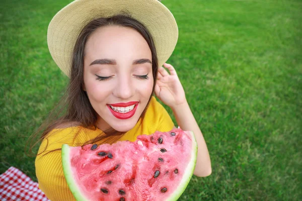 Beautiful young woman eating sweet watermelon in park