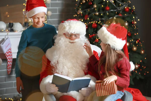 Santa Claus and little children reading book in room decorated for Christmas — Stock Photo, Image